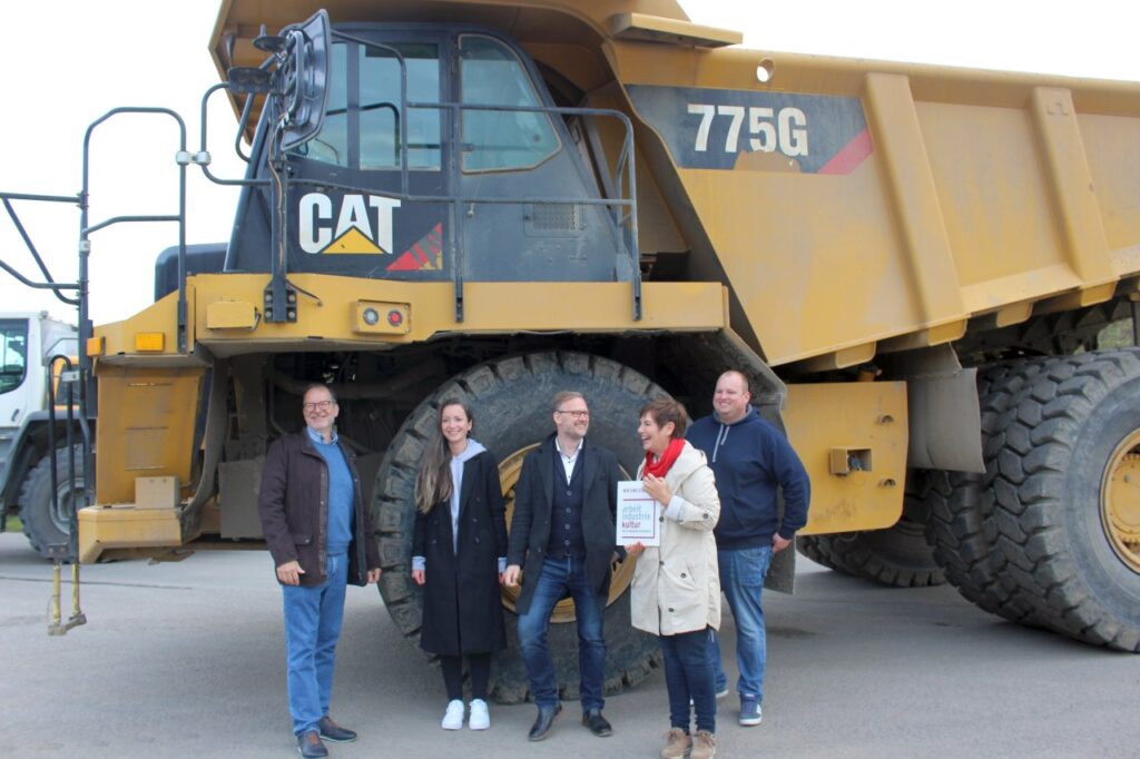 Moderne Technik an historischem Standort: Landrat Jens Womelsdorf (Mitte), Fachdienstleiter Dr. Markus Morr (li.) und Anna M. Becker (2.v.l.) vom Fachdienst Kultur und Sport des Landkreises Marburg-Biedenkopf, Dr. Bettina Nickel und Betriebsleiter Jan Engel vor dem gewaltigen 60-Tonner auf dem Gelände des Basaltwerks Nickel. (Foto: Landkreis Marburg-Biedenkopf/Heike Döhn)